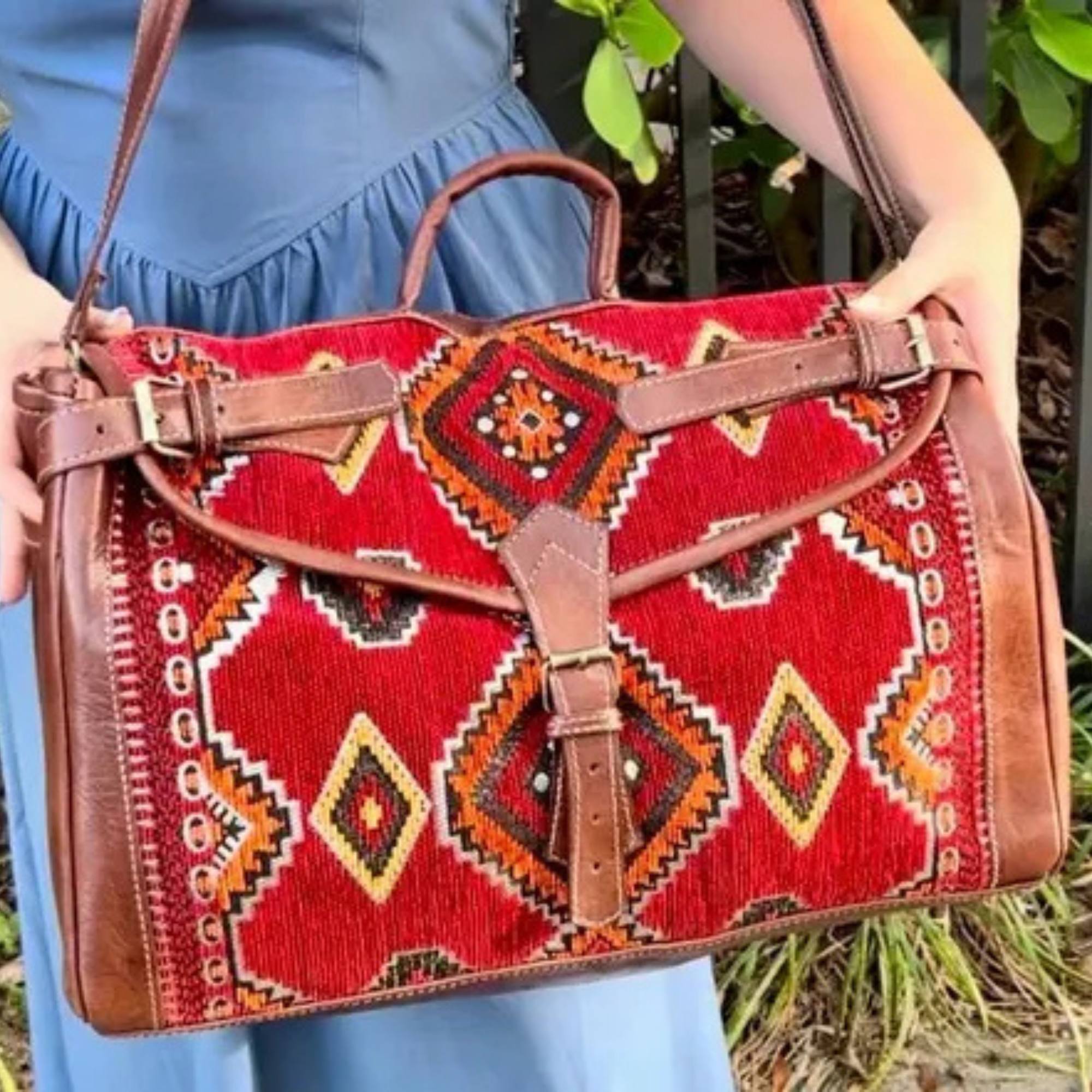 Person holding a red patterned handbag with brown leather straps.