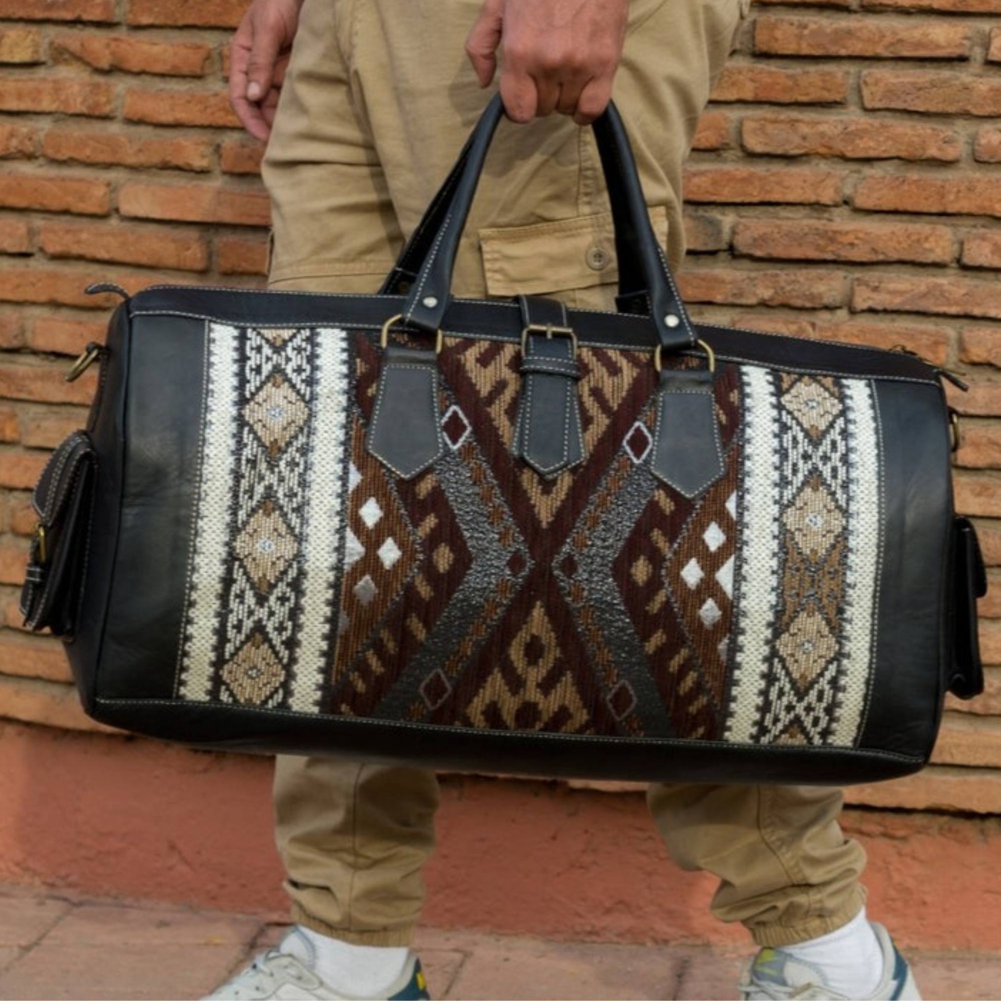 Person holding a patterned duffel bag against a brick wall.