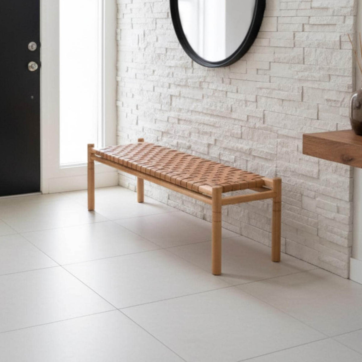 A modern wooden entryway bench with a woven rope seat, positioned against a white brick wall in a bright, contemporary room.