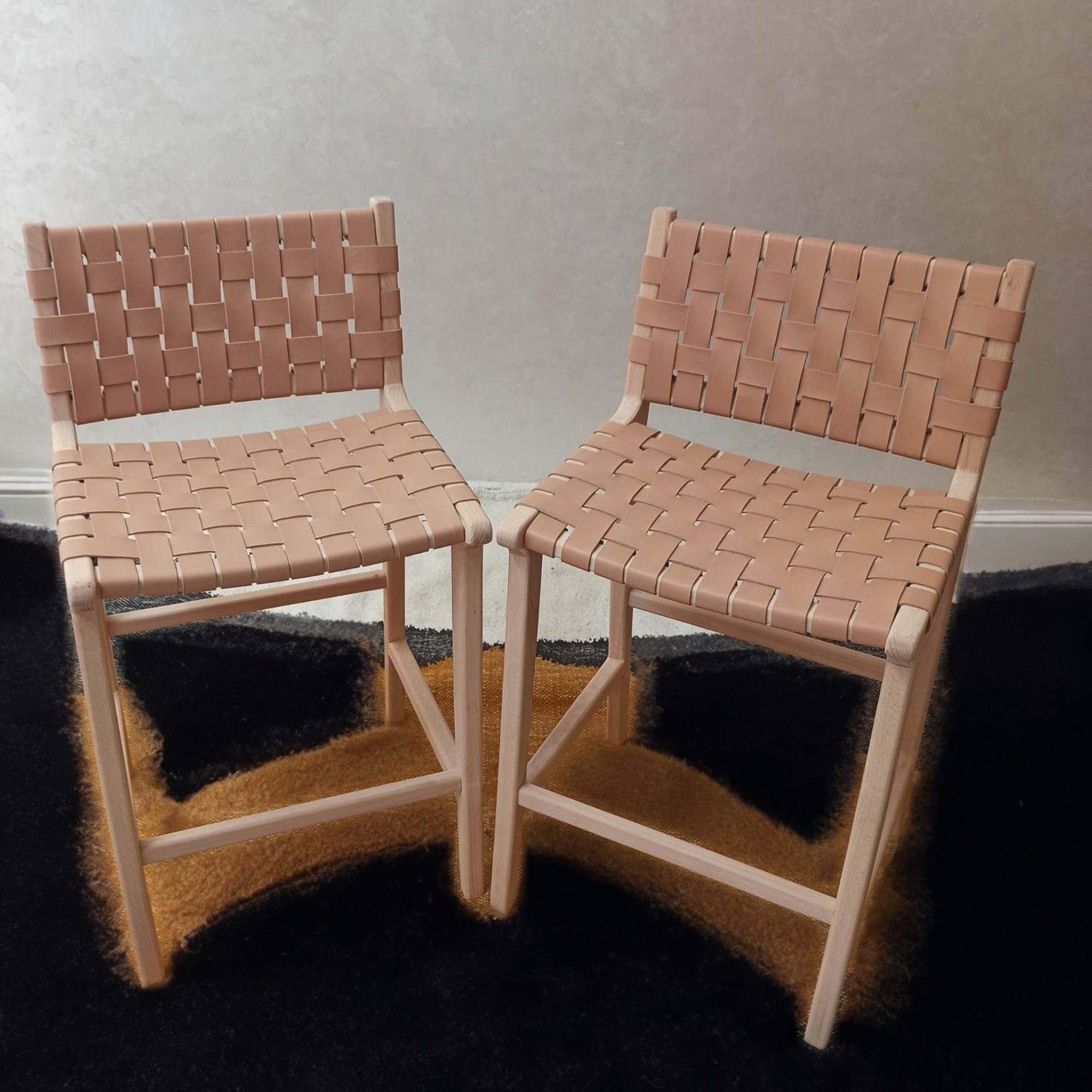 Two woven chairs on a dark rug with a neutral wall background