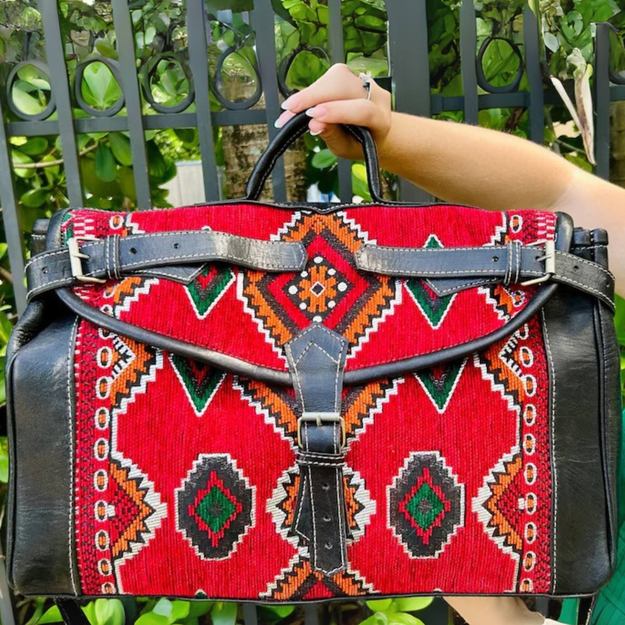 Red patterned bag held by a person with green foliage in the background