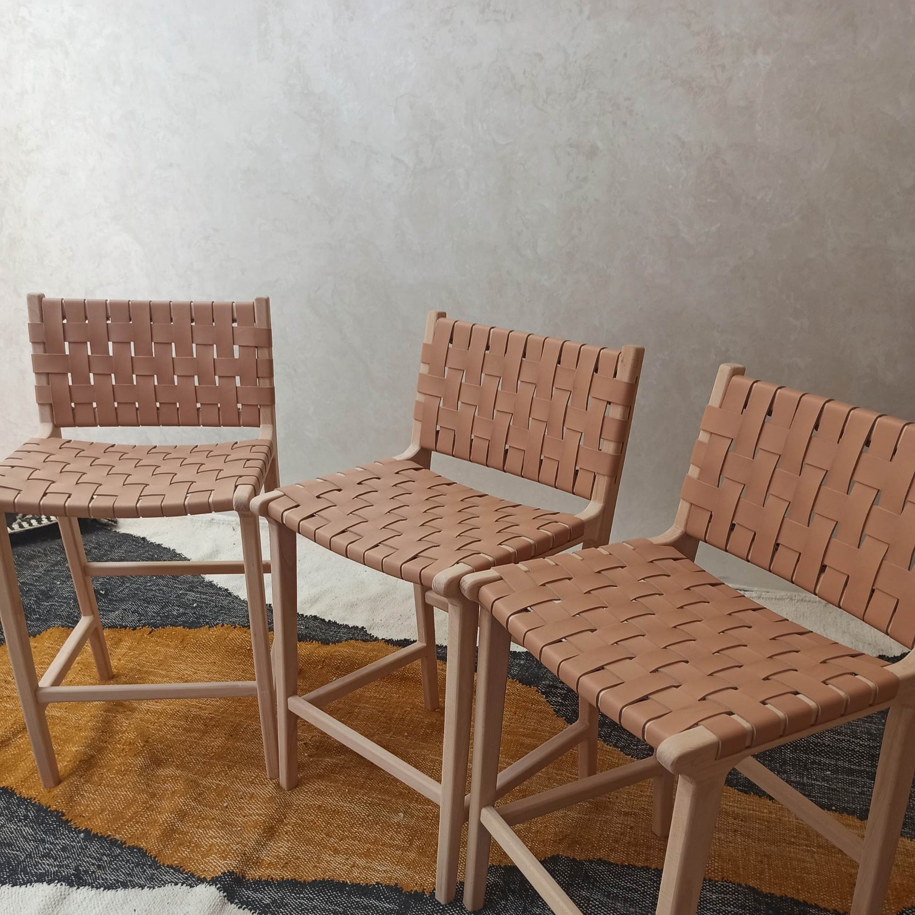 Three woven chairs on a textured rug with a neutral wall background