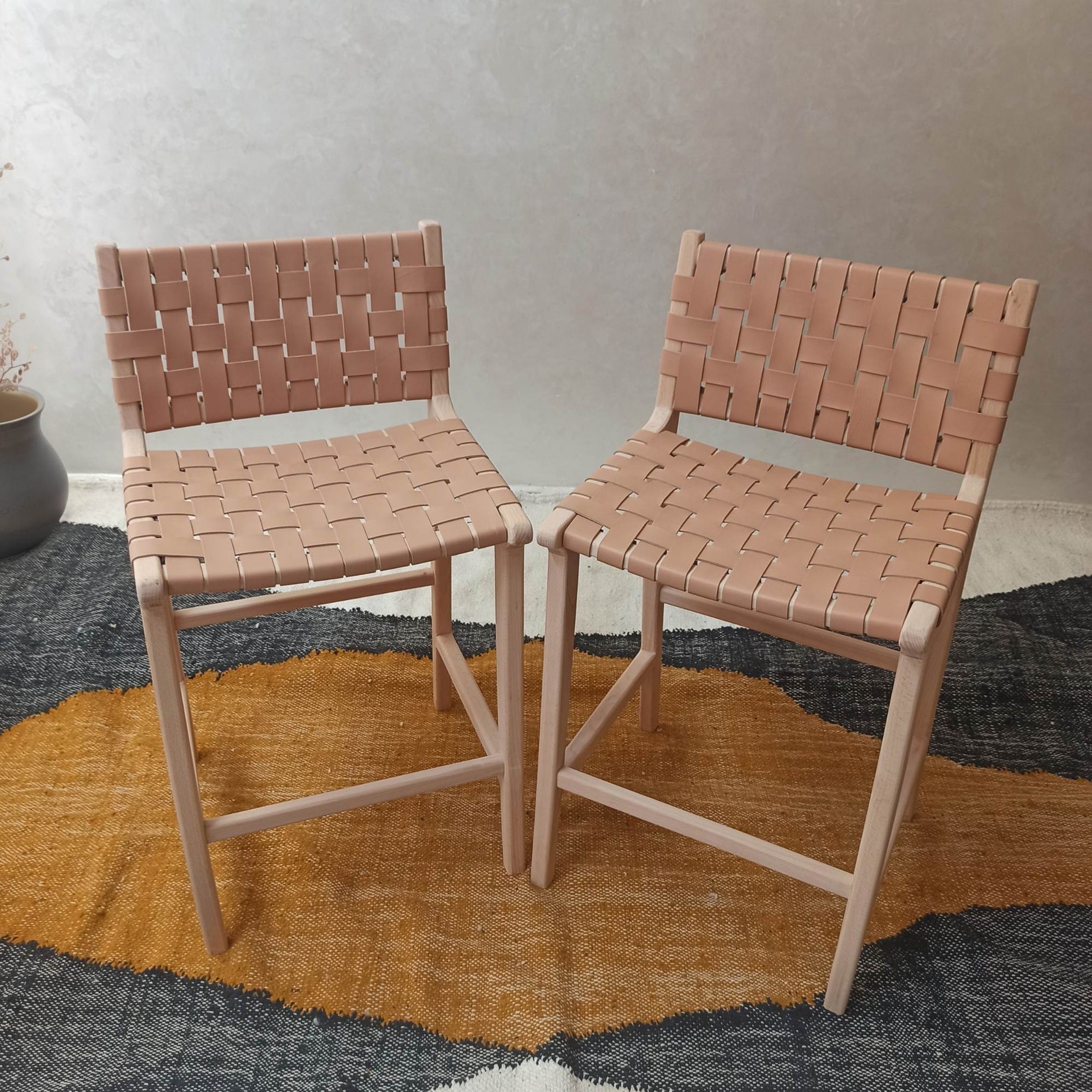 Two woven chairs on a textured rug with a neutral background