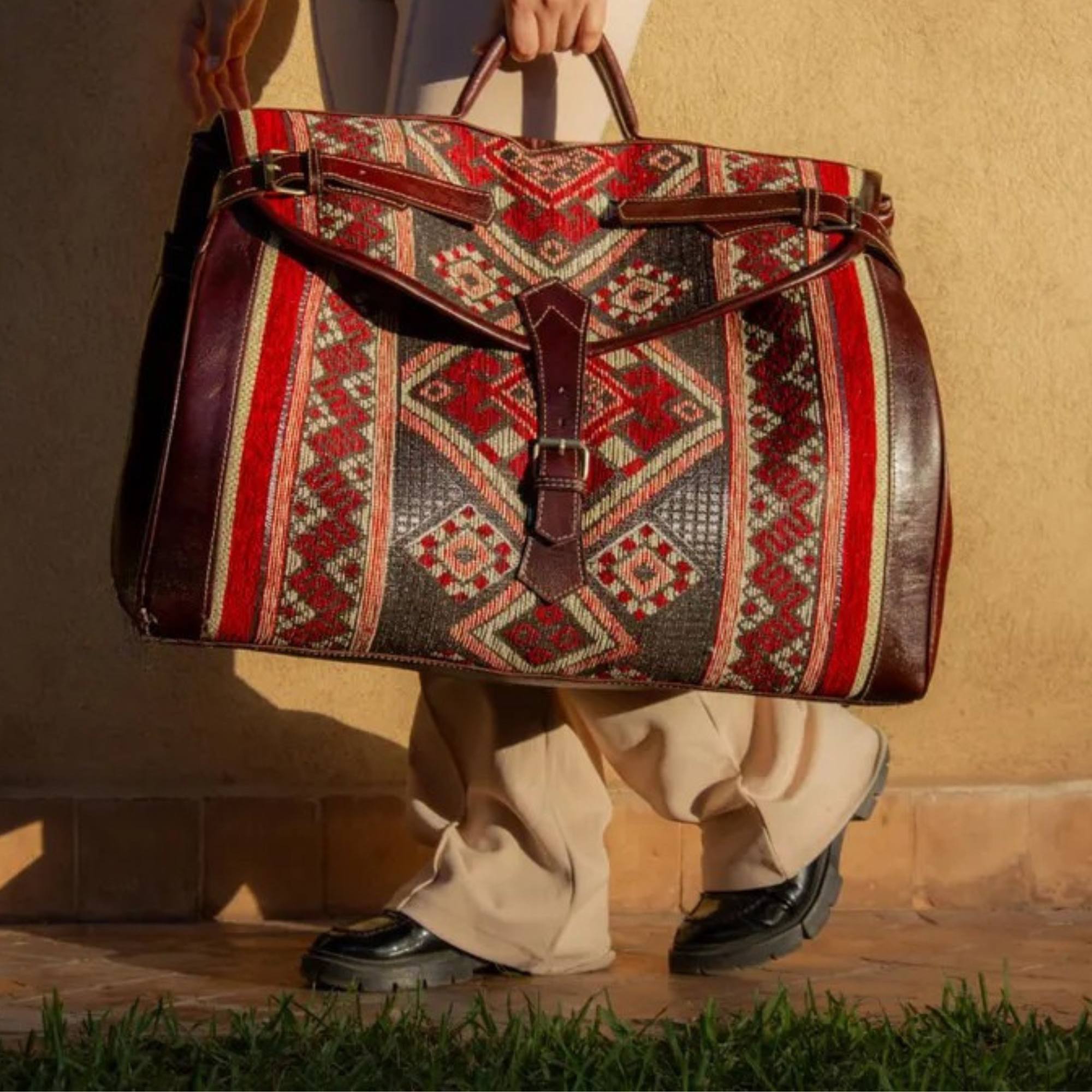 Person holding a large, patterned suitcase outdoors.