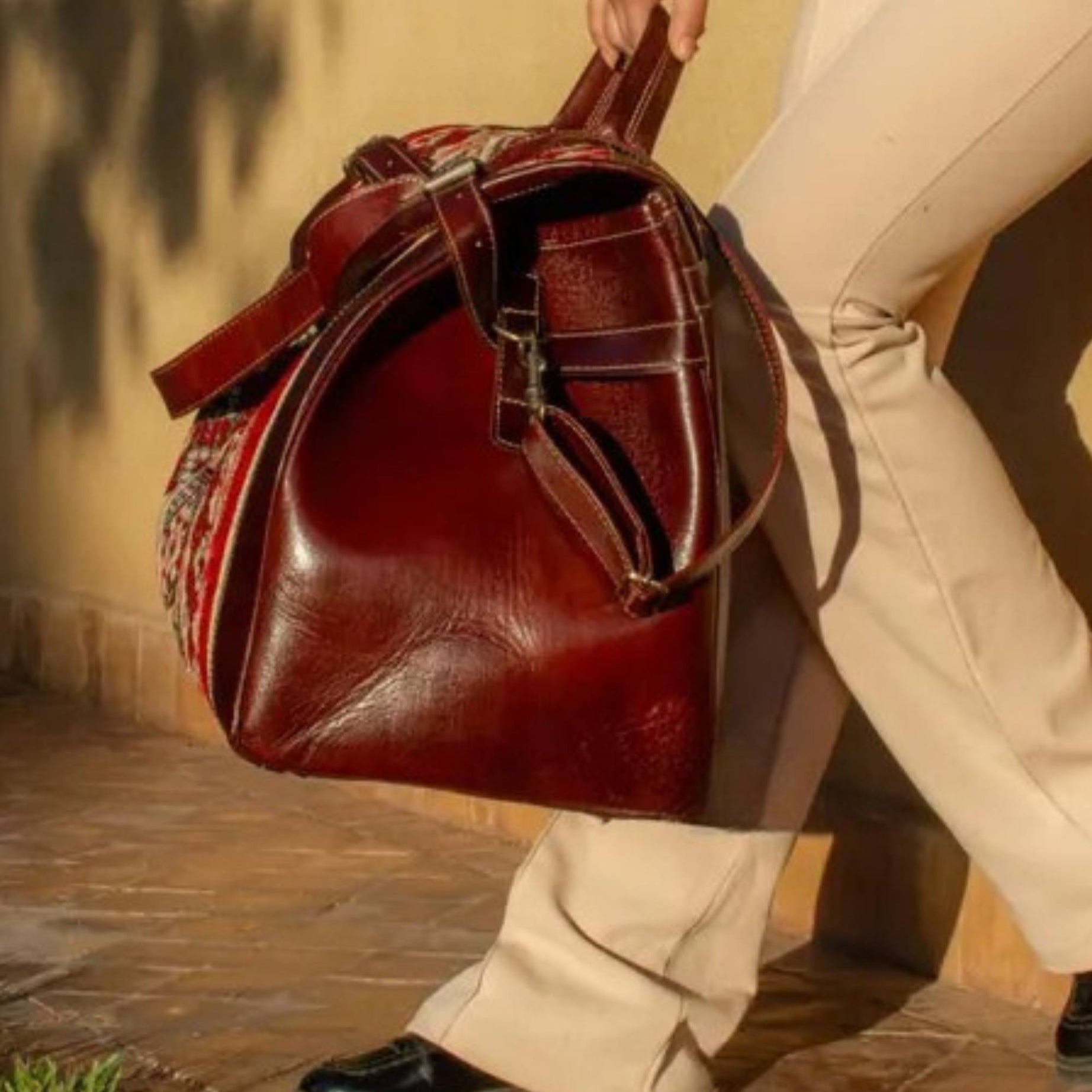 Person holding a large brown leather bag outdoors.