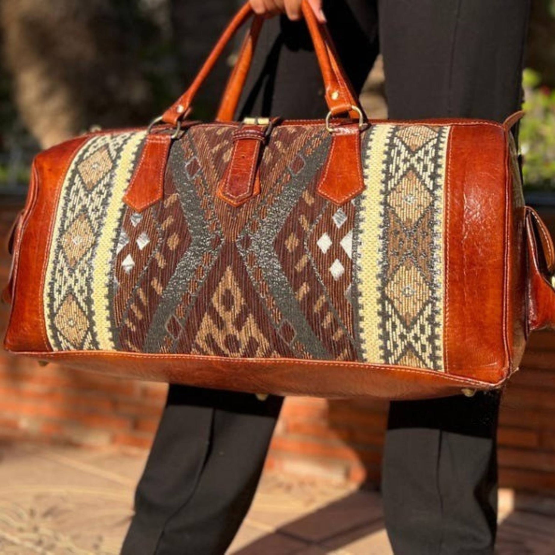 Brown leather bag with patterned design held by a person outdoors.