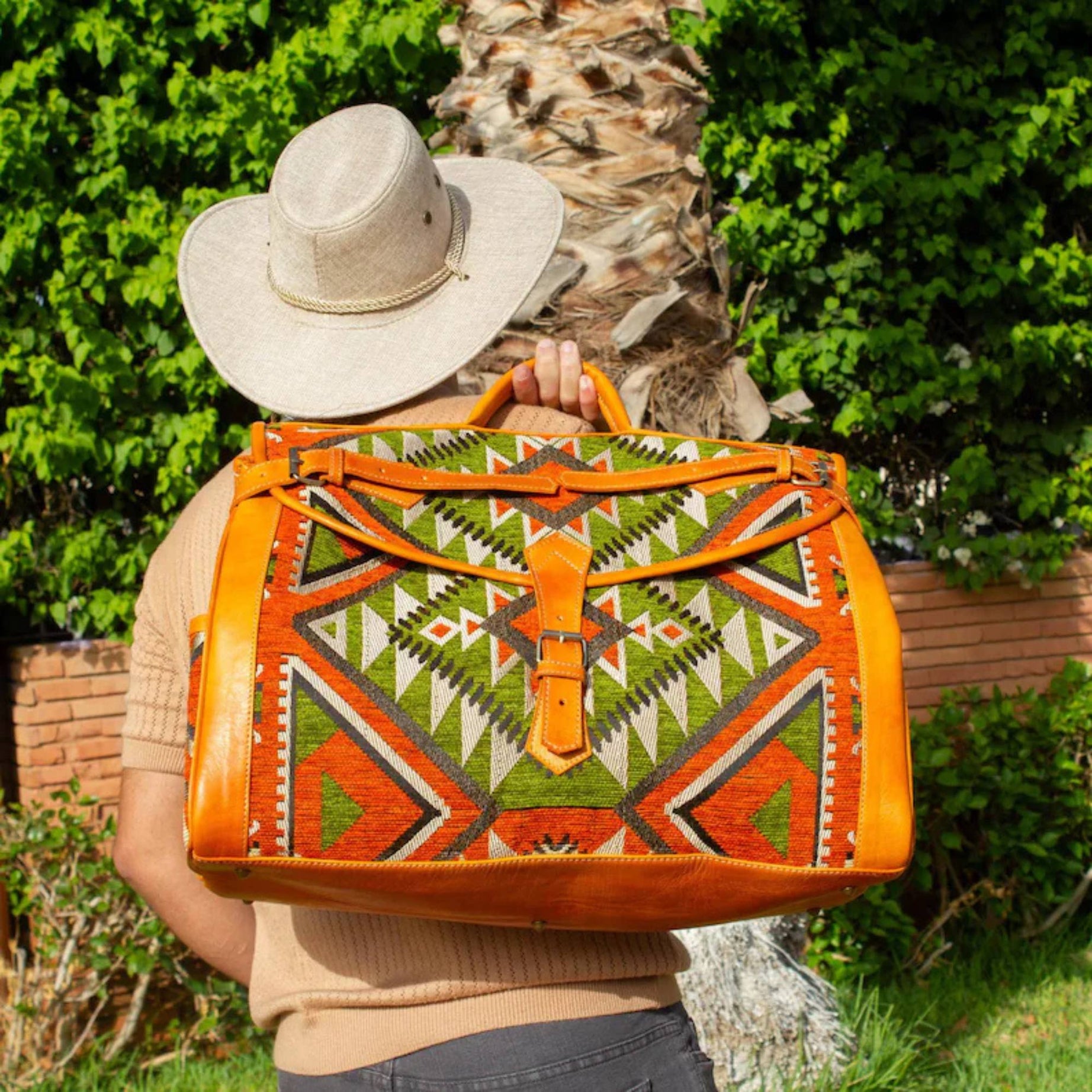 Person holding a colorful patterned bag outdoors with greenery in the background