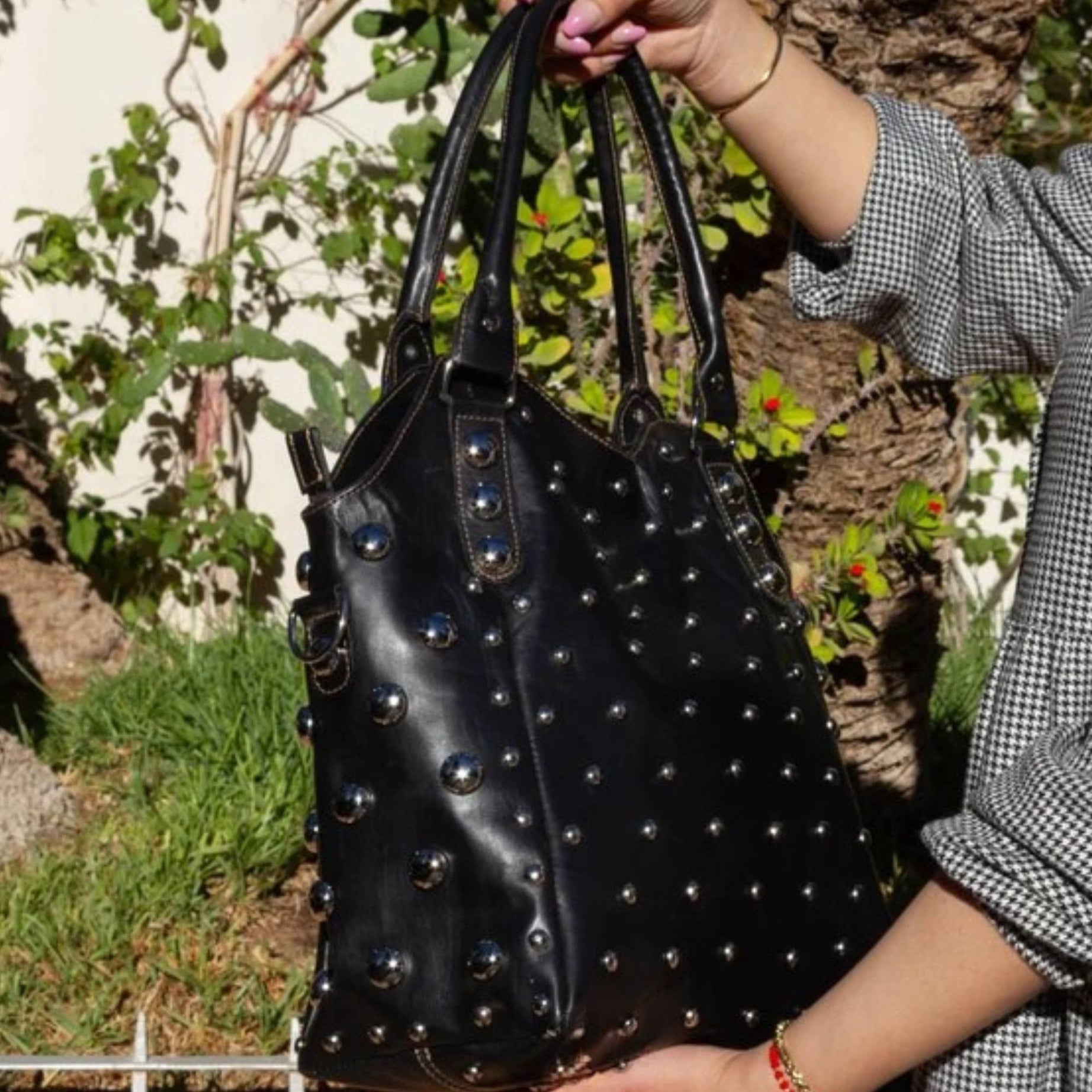 Black studded handbag held by a person outdoors