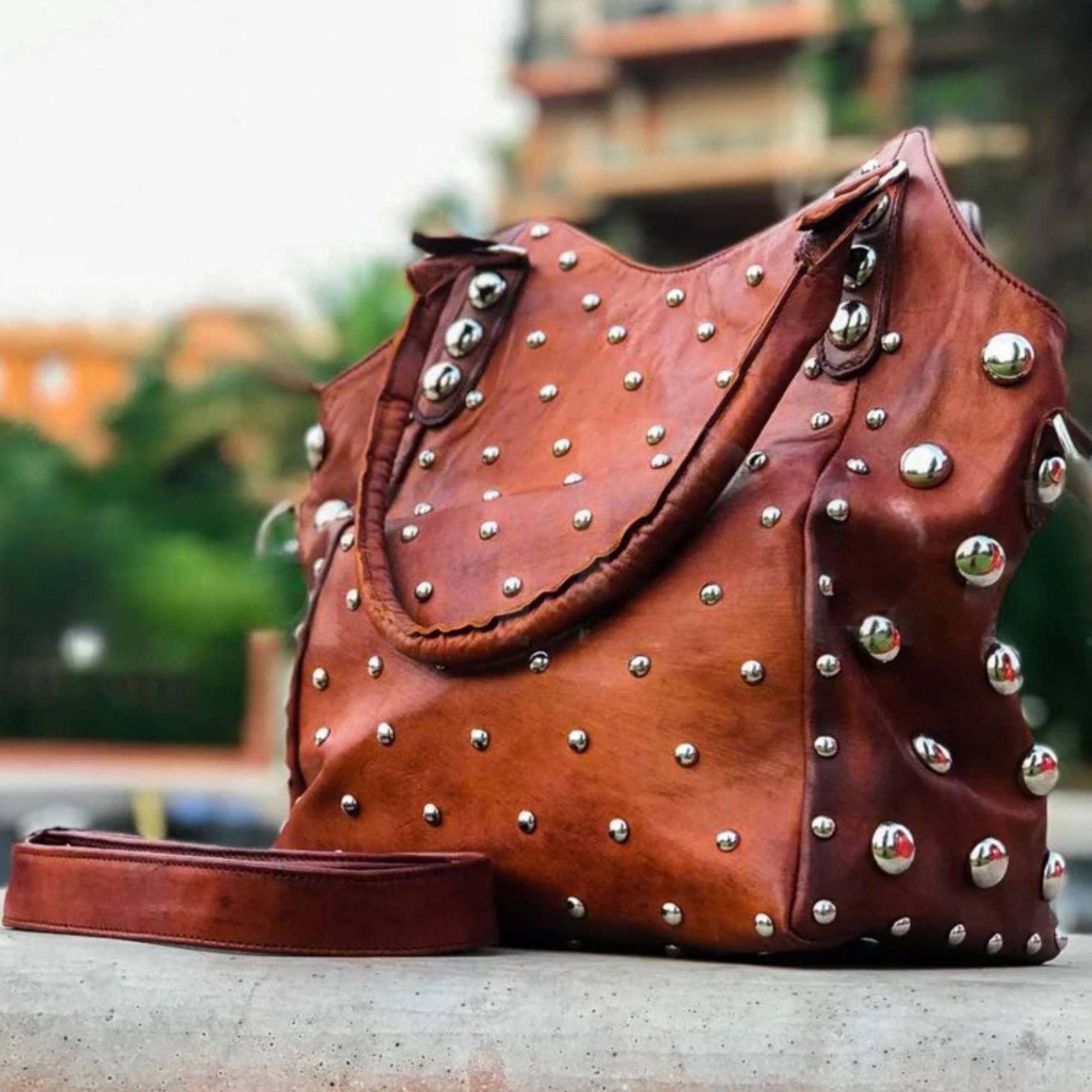 Brown leather handbag with silver studs on a blurred outdoor background