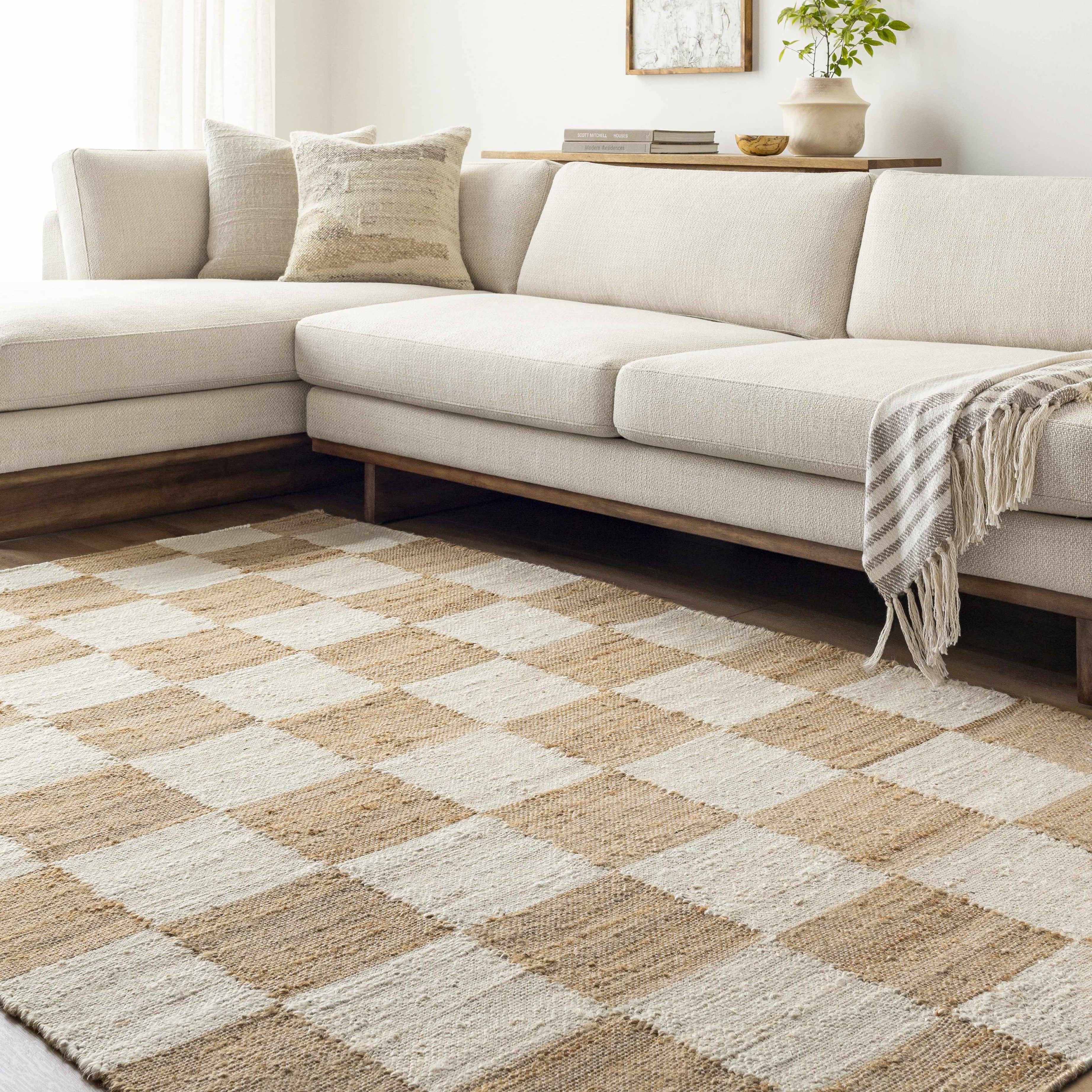 Beige and brown checkered rug in front of a white sectional sofa with cushions.
